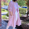 Person wearing a orchid purple long tunic coat outdoors with greenery and a building in the background