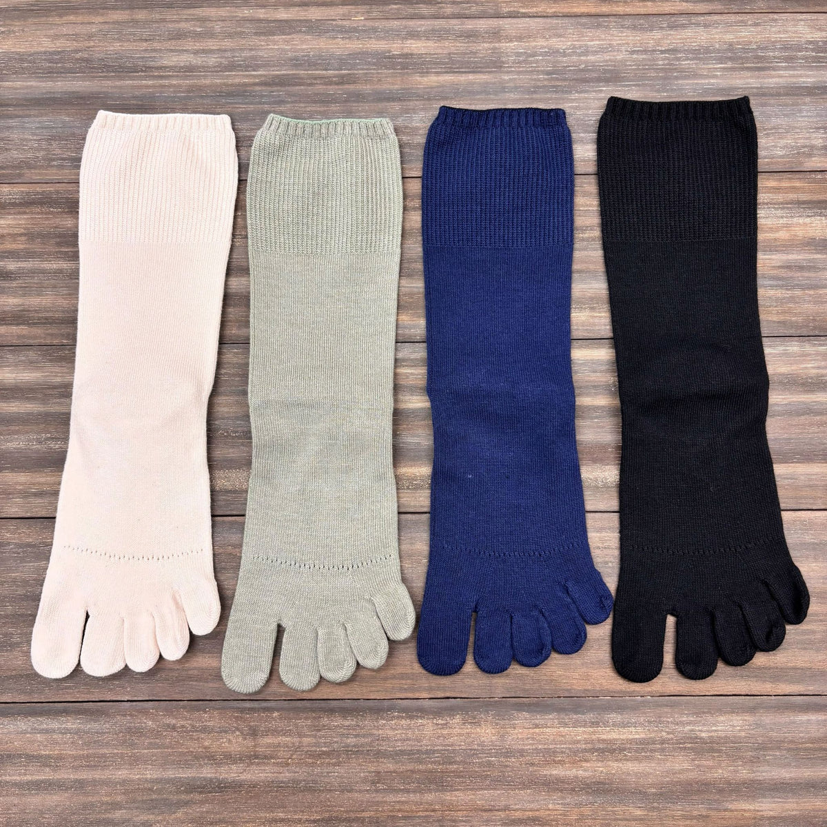 Four pairs of toe socks in white, green, blue, and black on a wooden surface.