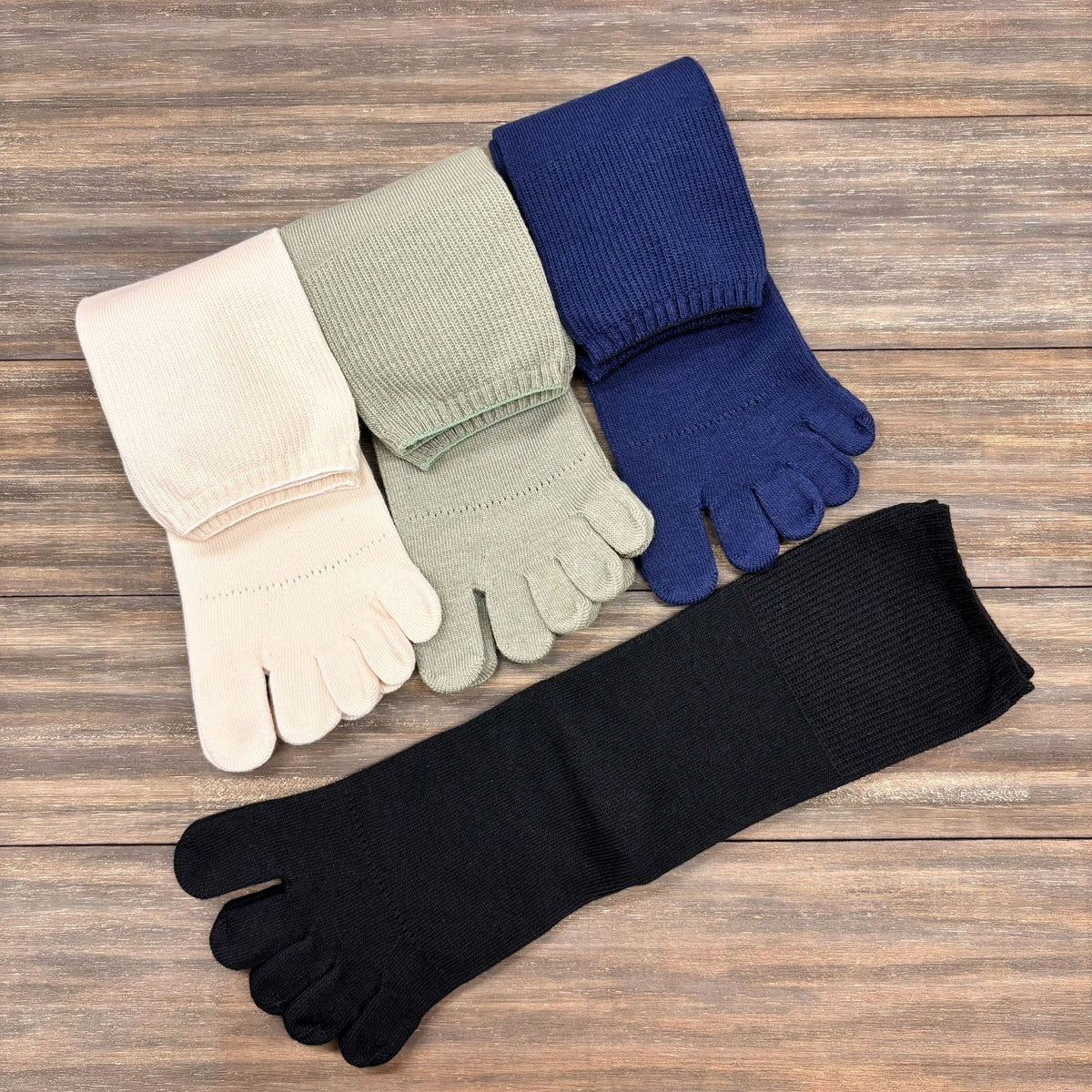 Set of five finger socks in black, blue, green, white, and navy on a wooden surface.