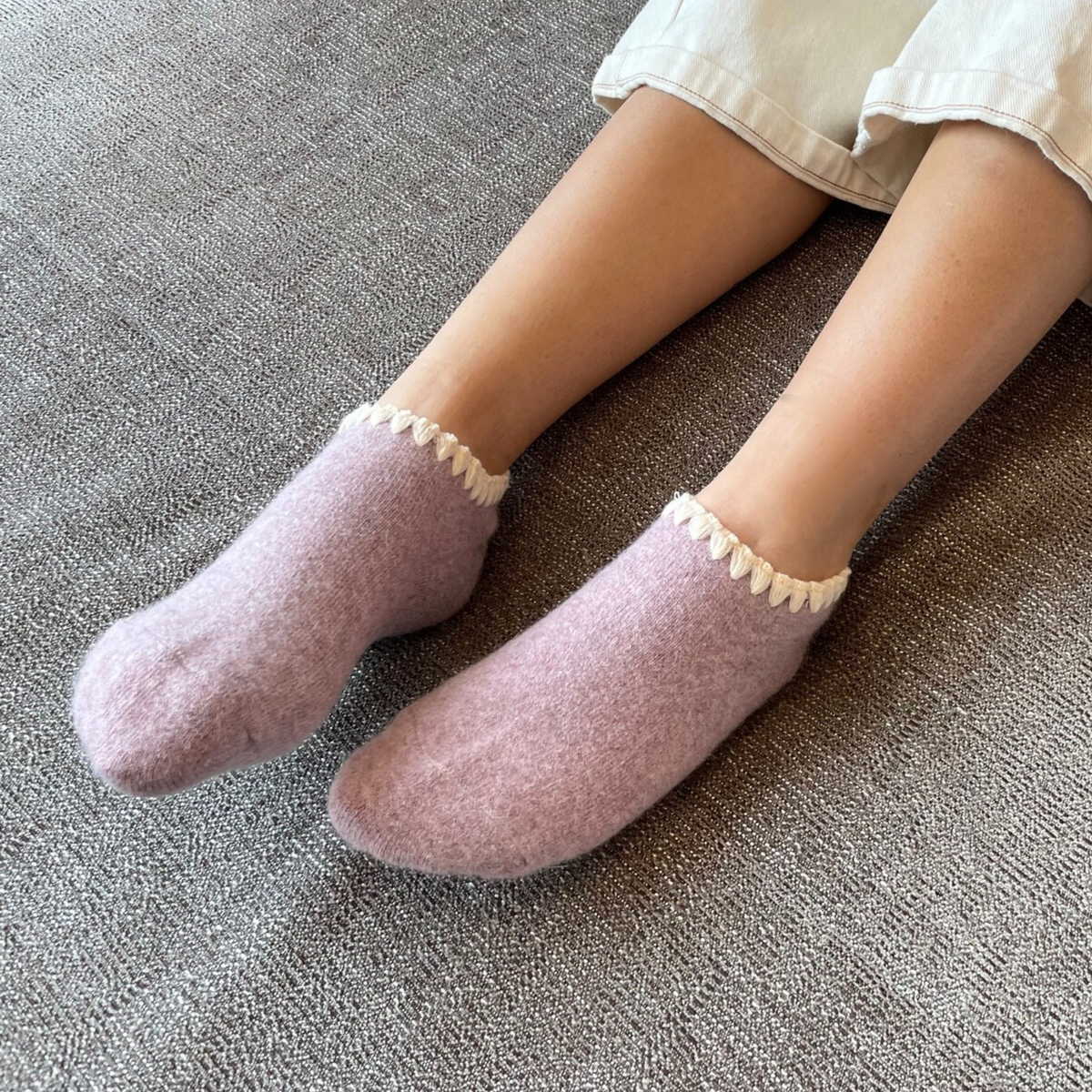 Angora Slipper Socks with anti-slip soles featuring transparent grip dots for extra safety. Each pair is handcrafted, incorporating traditional craftsmanship, and finished with cherrystone shell-shaped embroidery on the sock opening. Soft, cozy, and comfortable for ultimate foot pampering.