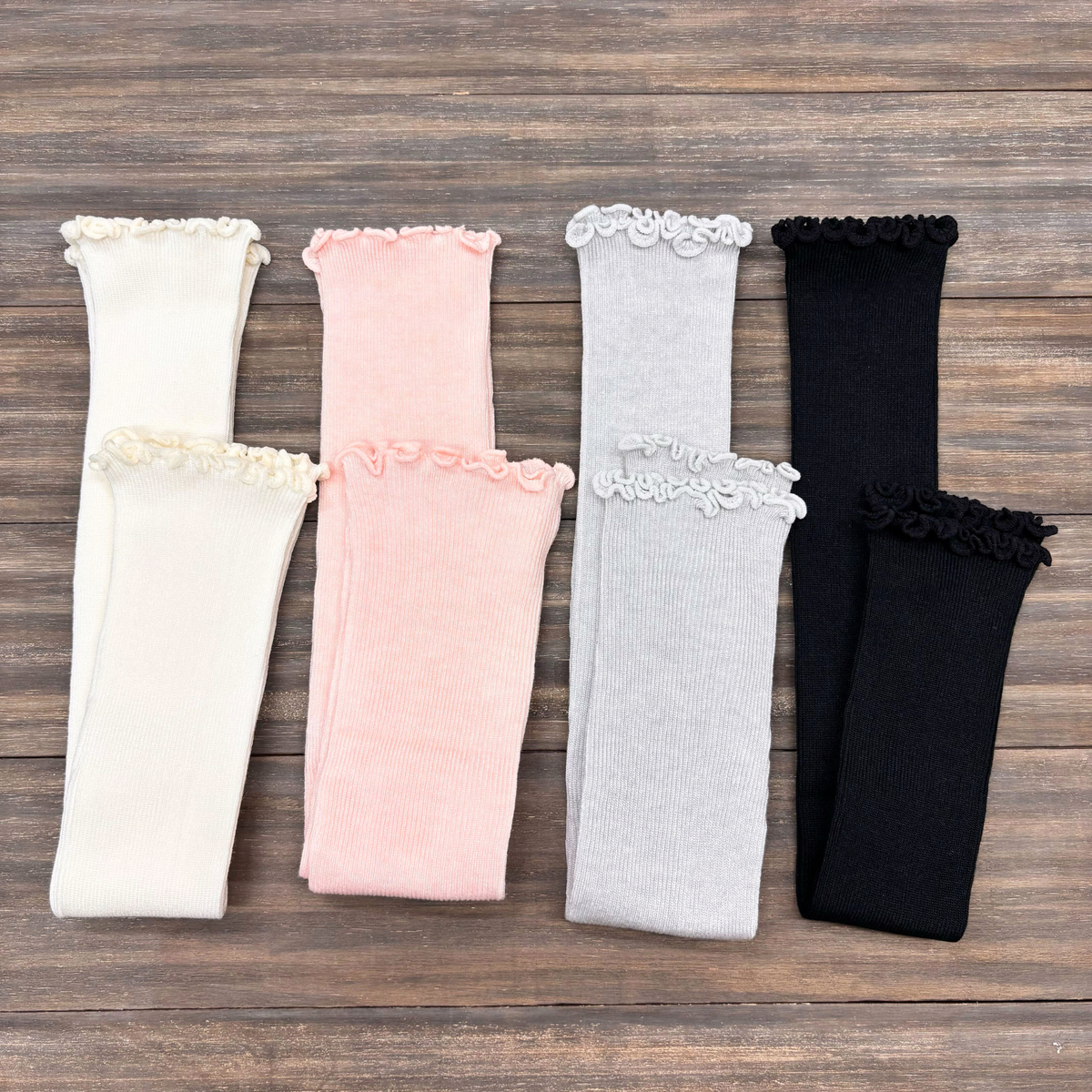 Four pairs of arm covers in white, pink, gray, and black on a wooden surface.