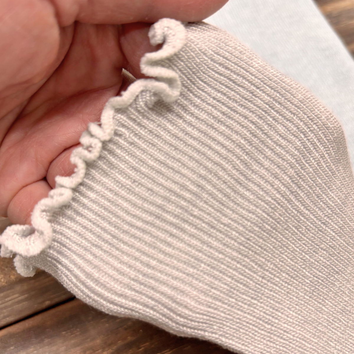 Close-up of a white arm cover with white trim held by a hand on a wooden surface.