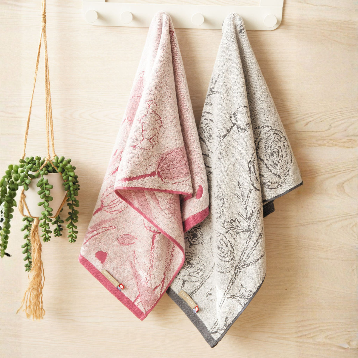 Two patterned towels hanging on a wooden surface with a plant in the background.