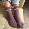 Dull pink socks with white trim worn by a person sitting on a beige couch.