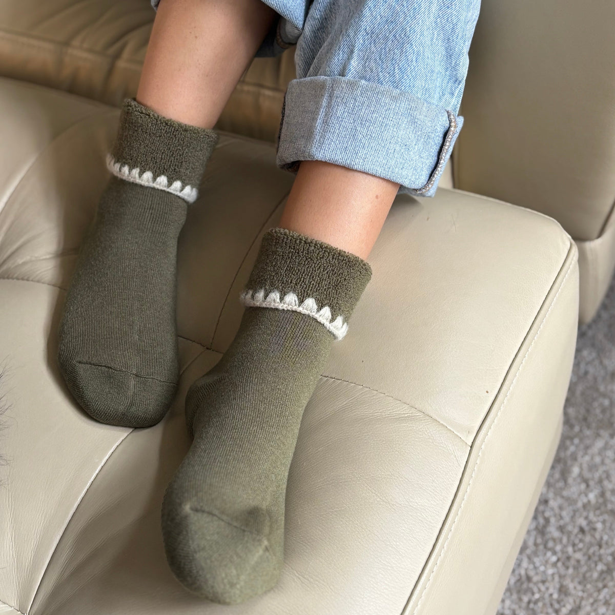 Person wearing olive green socks with white trim on a beige couch.