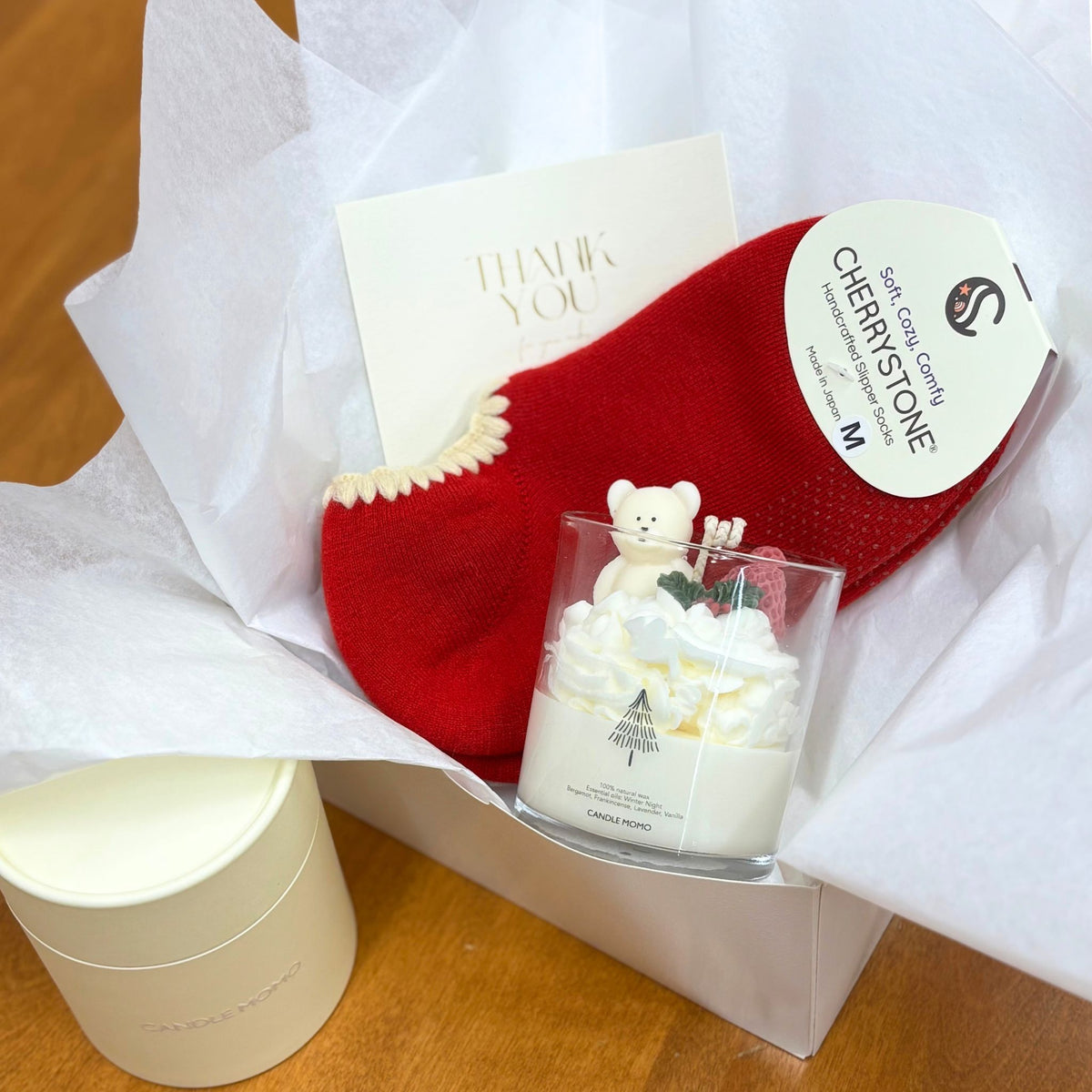 Red socks with a white label and a candle in a glass holder with a bear design on a white surface.