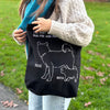 Person holding a black tote bag with dog illustrations and text in an outdoor setting.