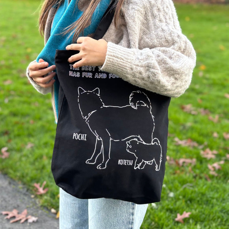Person holding a black tote bag with dog illustrations and text in an outdoor setting.