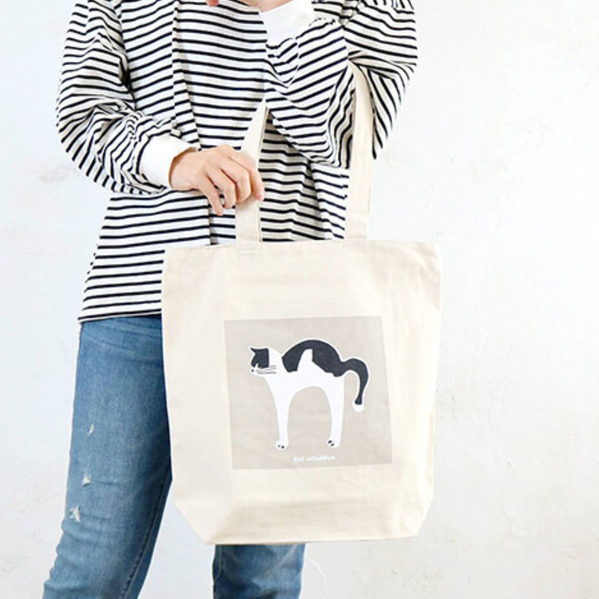 A model has a tote bag that is made of recycled fabric, with a stretching-cat design.