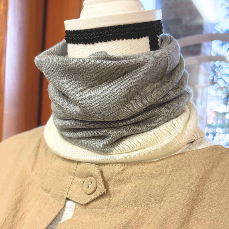 Mannequin wearing a beige coat with a gray neck warmer and a black and white striped headband.