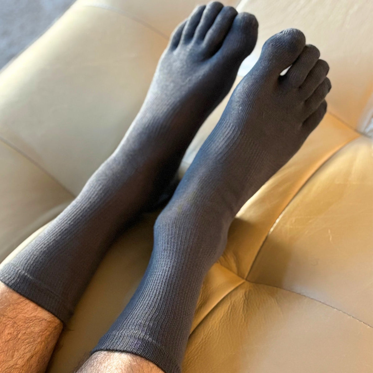 Gray socks worn on feet with a beige chair in the background