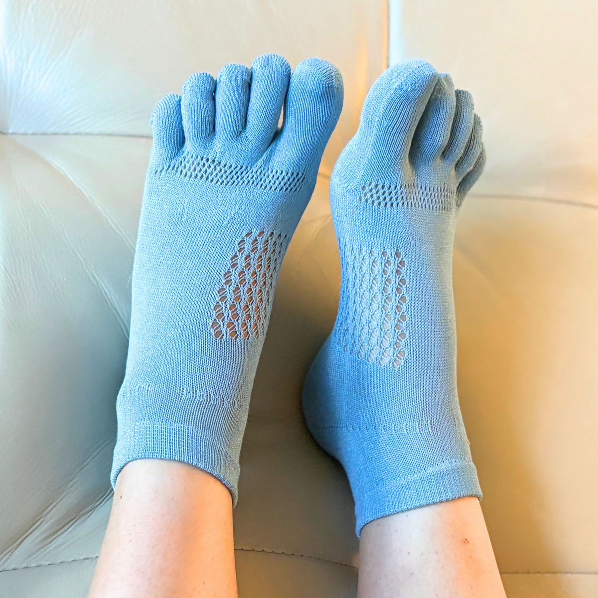 Blue five-finger socks worn on a person's feet with a neutral background