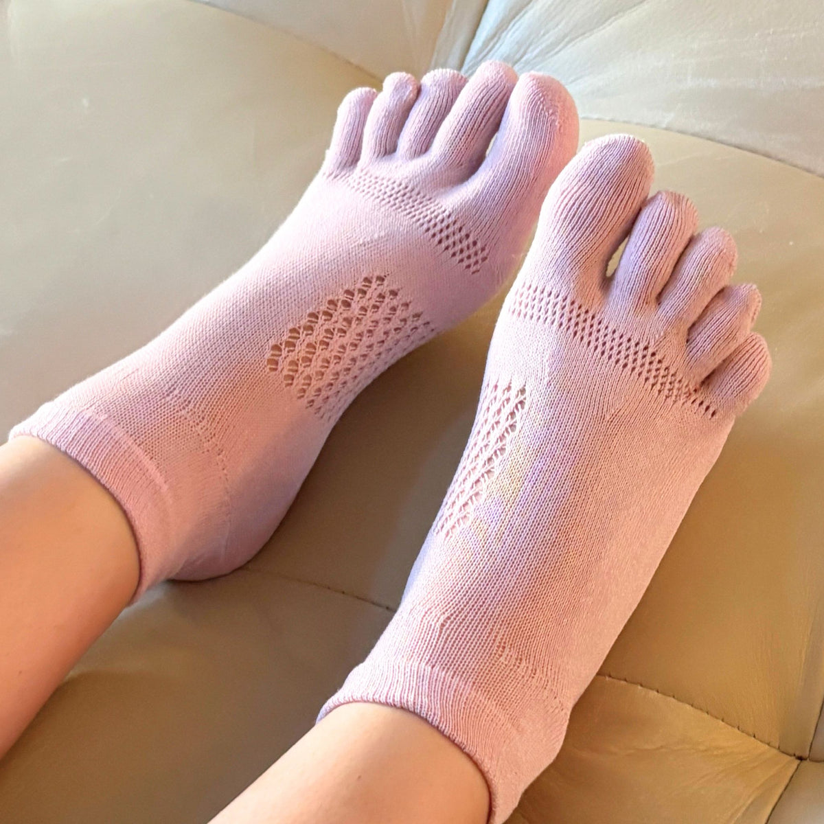 Pink toe-separated socks worn on a beige surface