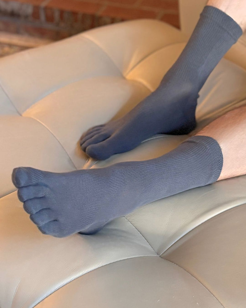 A person wearing dark slate blue toe socks sitting on a cream tufted leather couch.