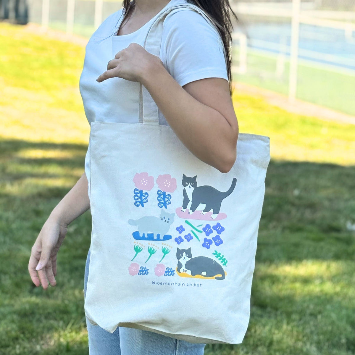 Person holding a tote bag with cat and flower designs outdoors.