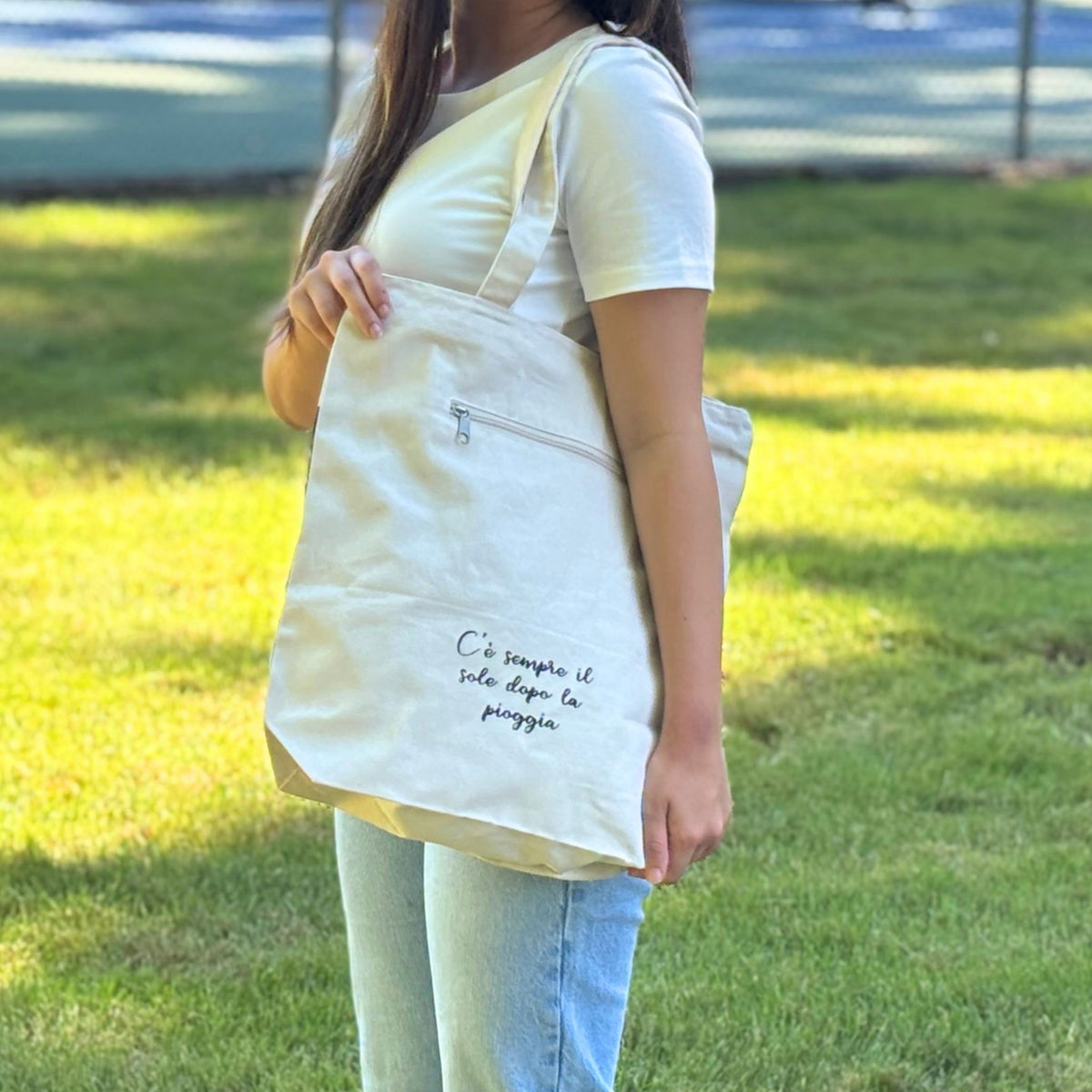 Person holding a beige tote bag with text in an outdoor setting