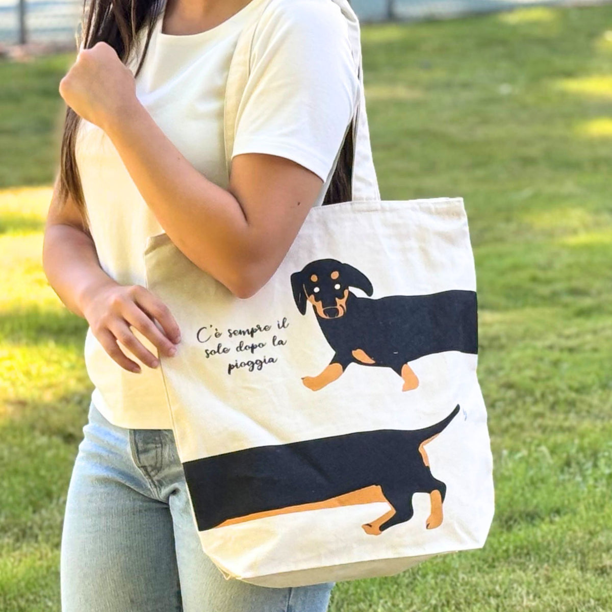 Person holding a tote bag with dachshund design and text outdoors