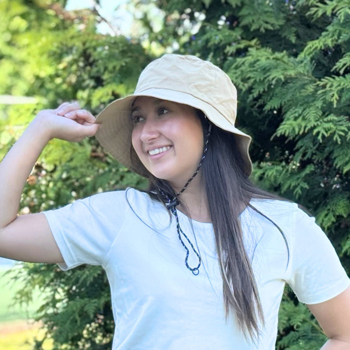 Woman wearing a beige bucket hat outdoors with greenery in the background