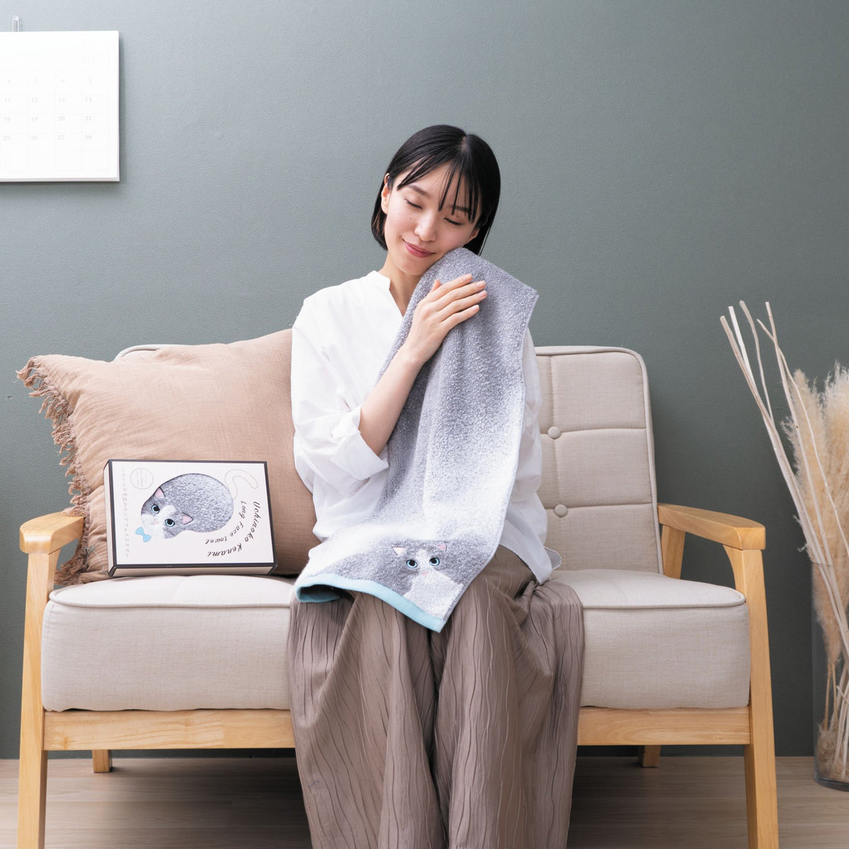 Woman sitting on a couch holding a face towel with a gray wall and decorative elements in the background