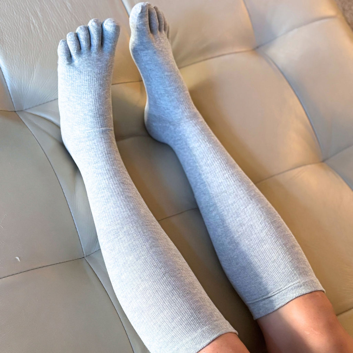 Gray knee-high socks worn by a person sitting on a beige couch.