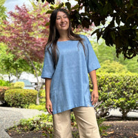 woman wearing a blue shirt and beige pants standing outdoors.