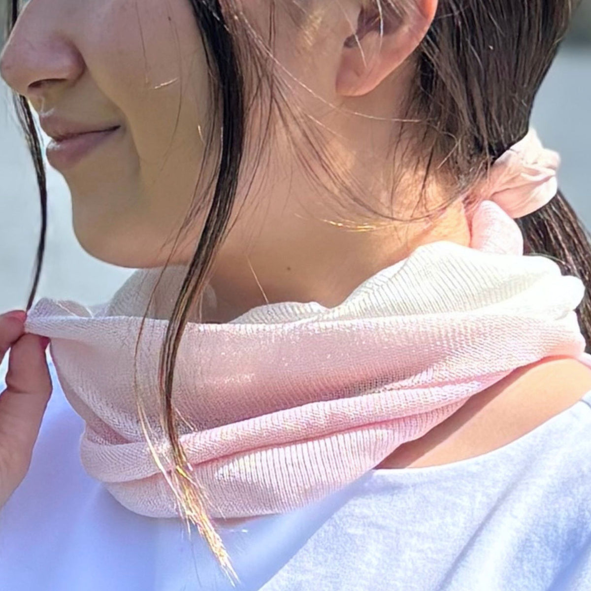 Close-up of a person wearing a pink silk neck warmer with a blurred background