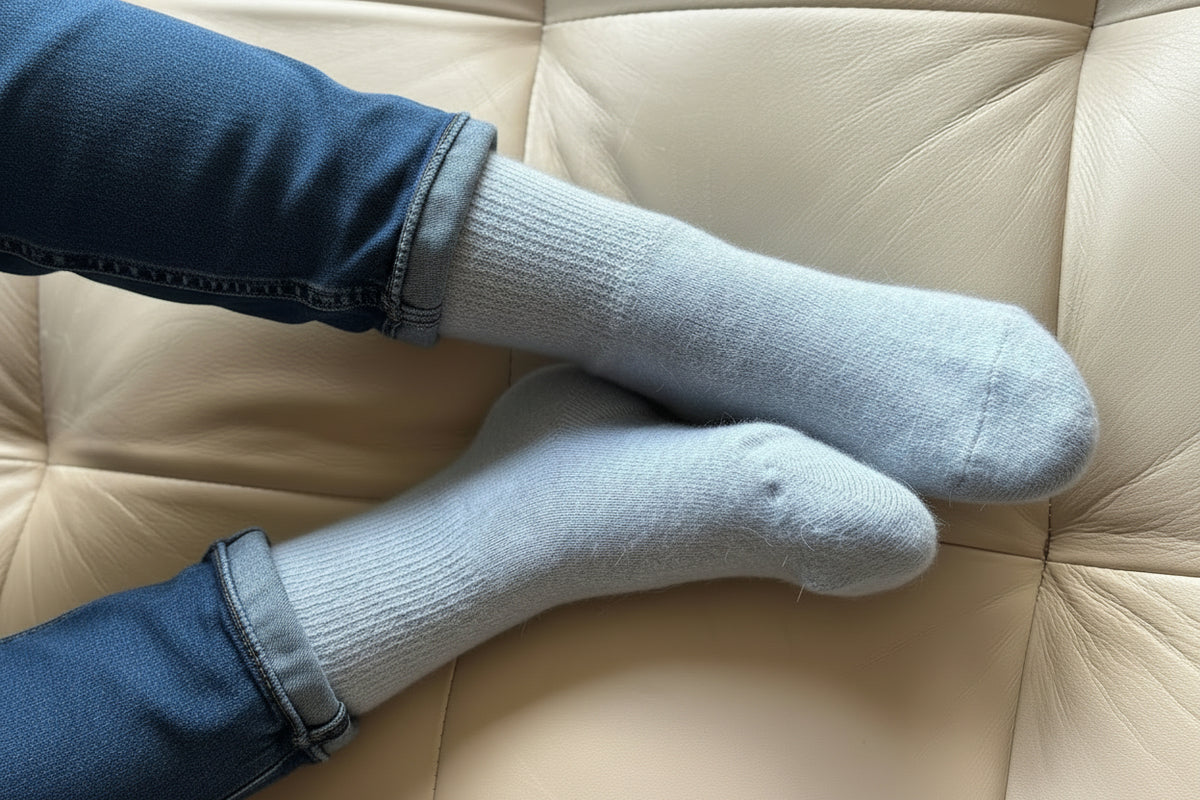 A pair of light blue ribbed knit socks worn on feet, resting on a beige leather tufted chair.