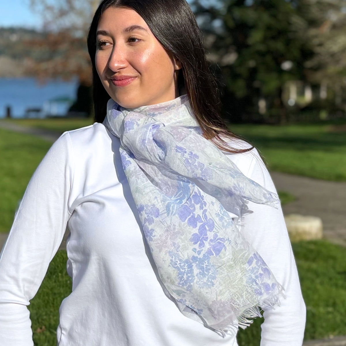 Woman wearing a floral scarf outdoors with a lake and trees in the background