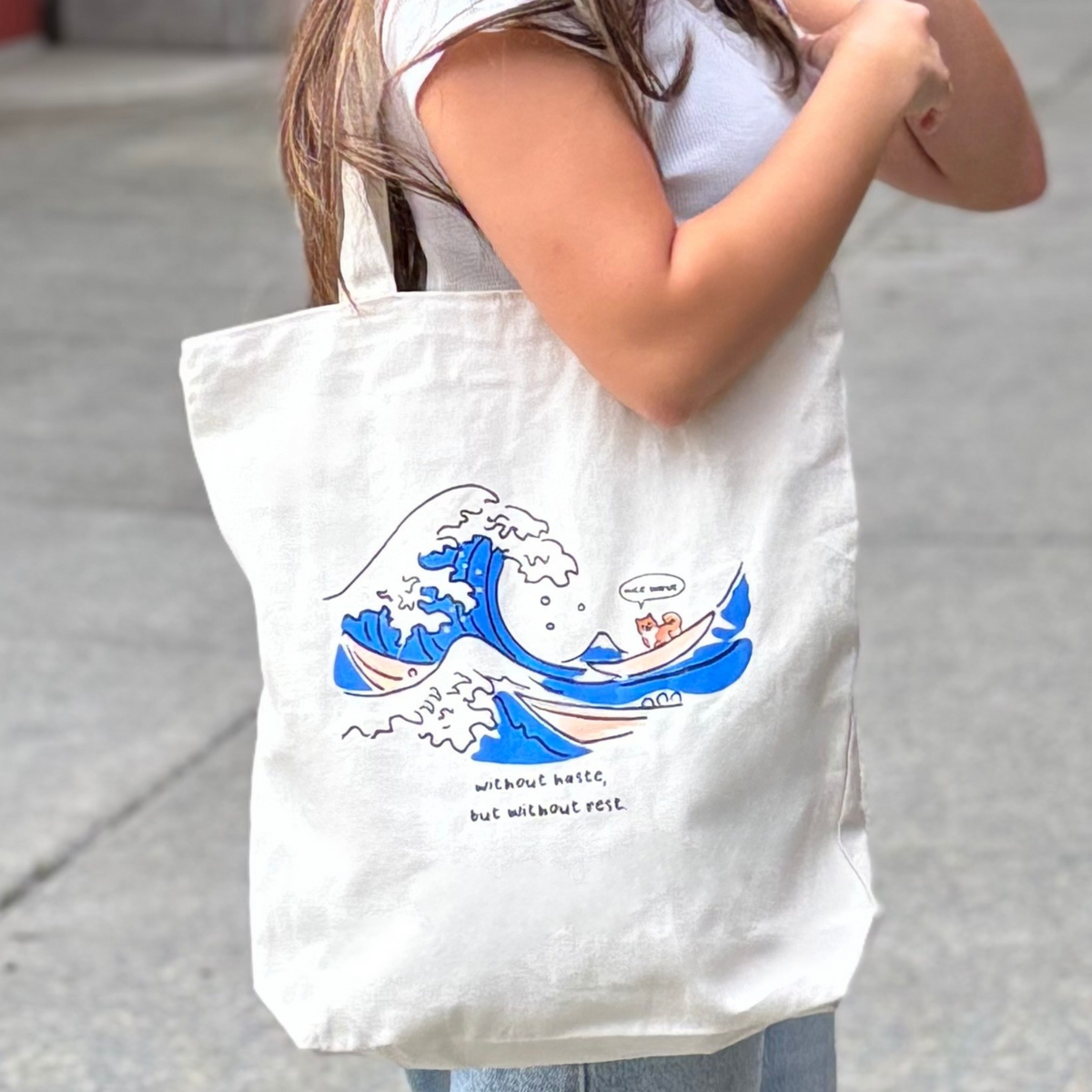 Person holding a tote bag with a wave design and text.