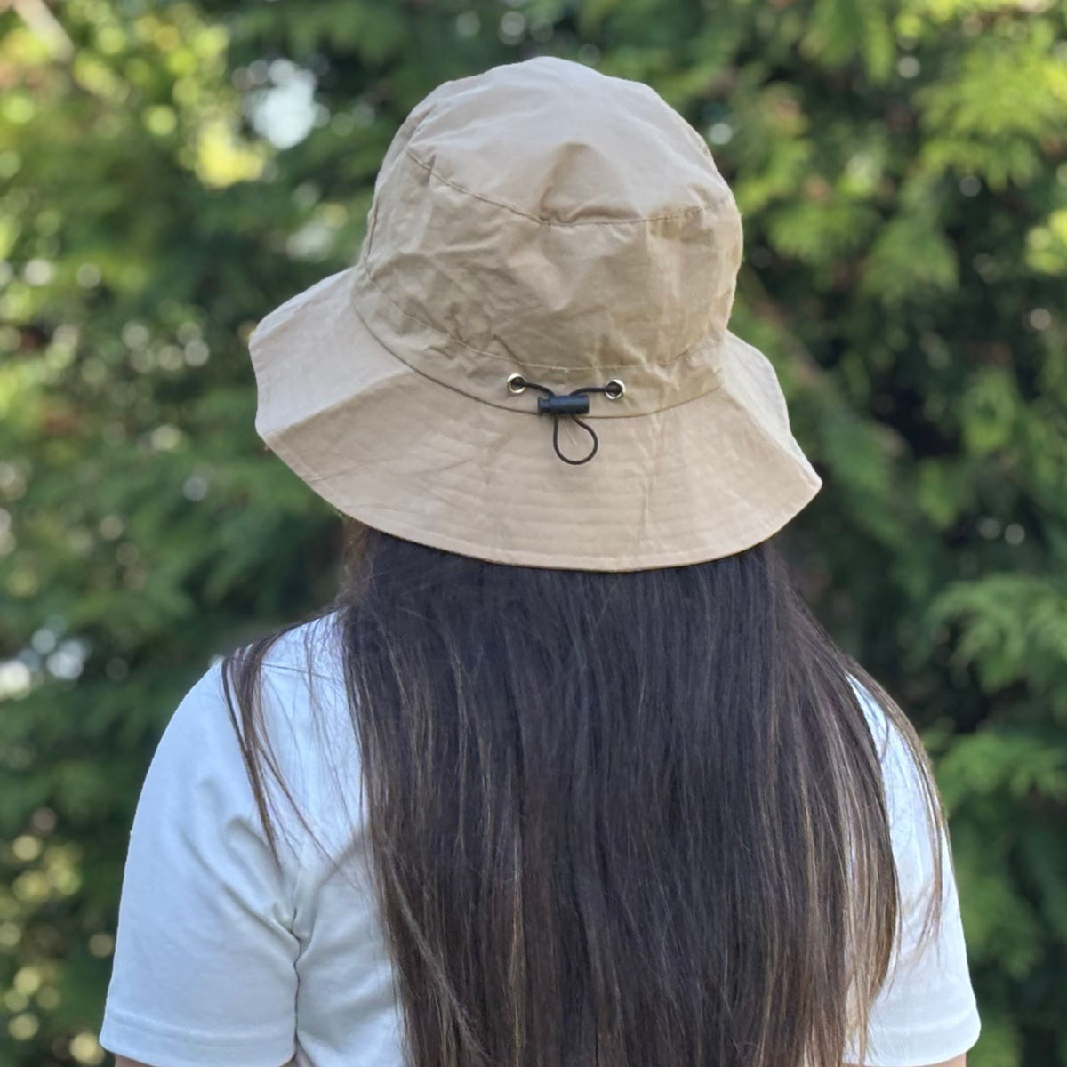 Person wearing a beige bucket hat with a blurred green background
