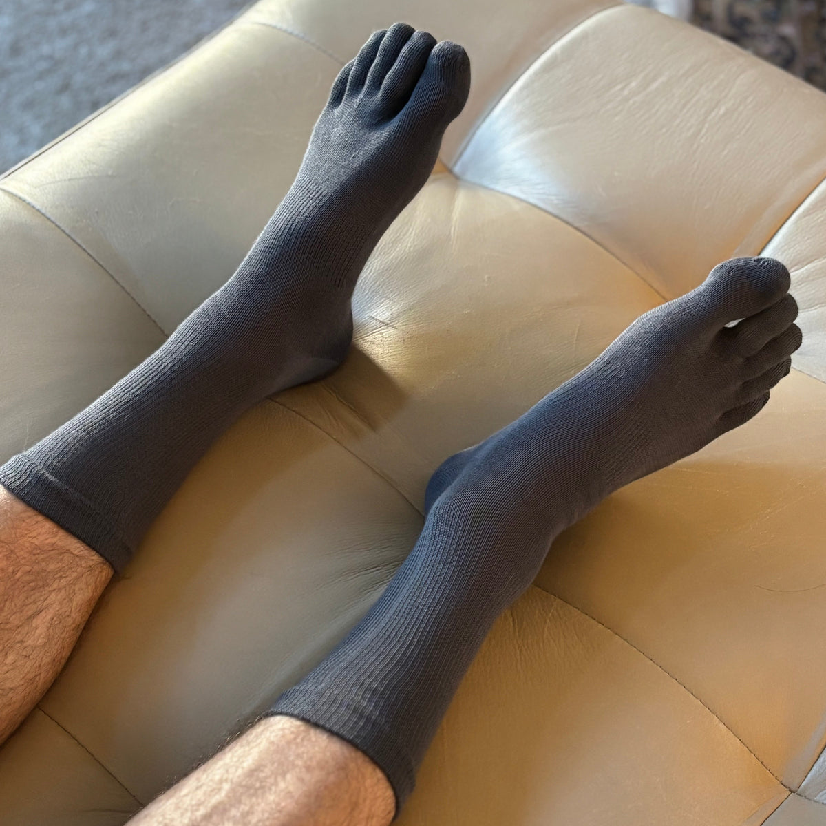 Person wearing dark gray 5-toe socks on a beige couch