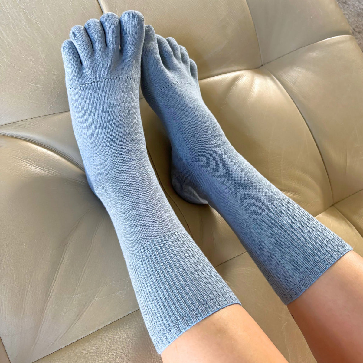 Blue toe-separated socks worn on a beige sofa