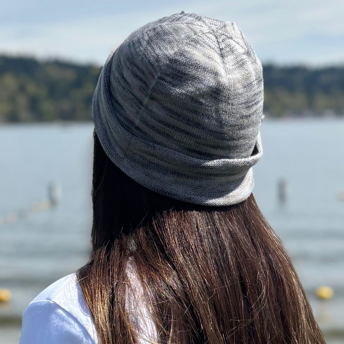 a Person wearing a gray silk beanie with a blurred lake and trees in the background
