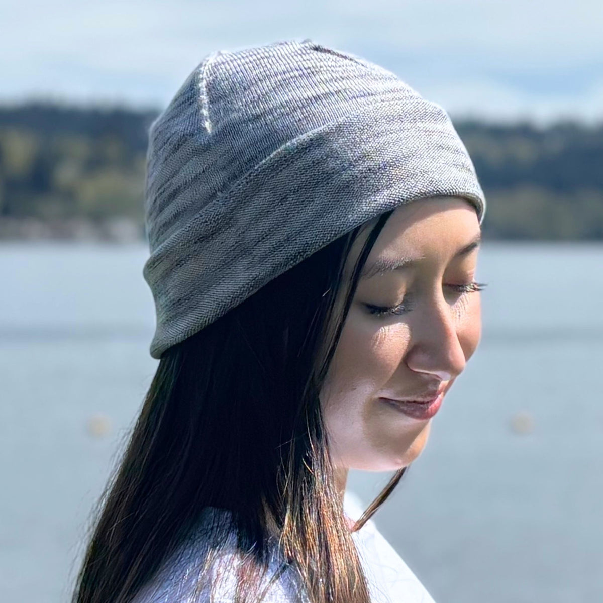 A woman wearing a gray silk beanie by a body of water