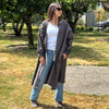 Person wearing a long coverall trench coat and in a park-like setting