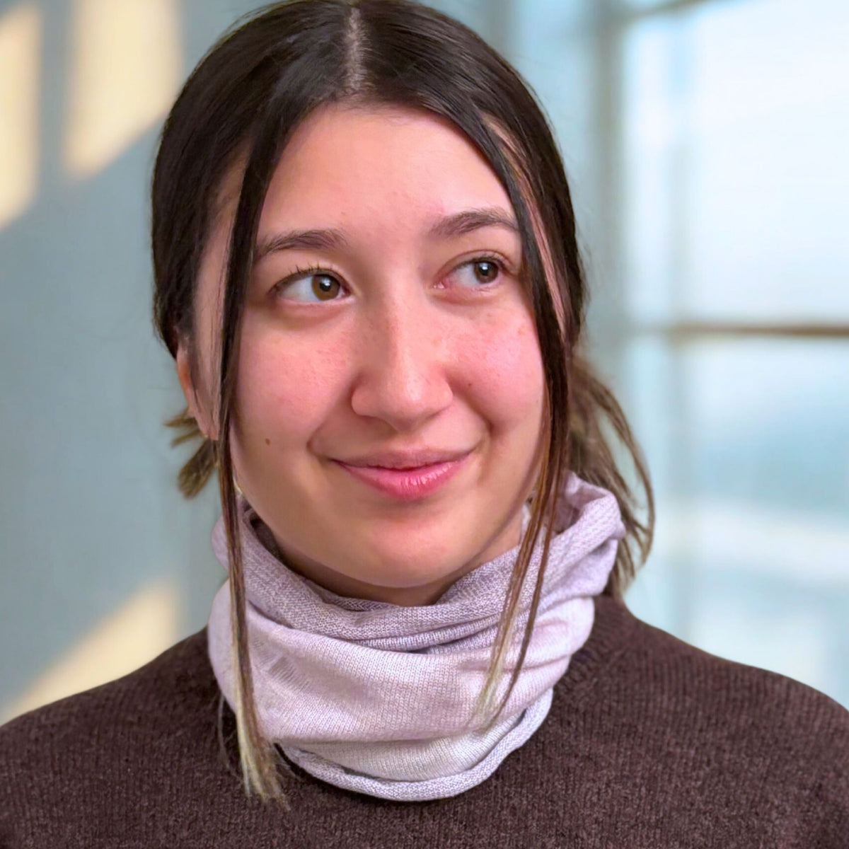 Woman wearing a brown sweater and light purple scarf with a blurred background