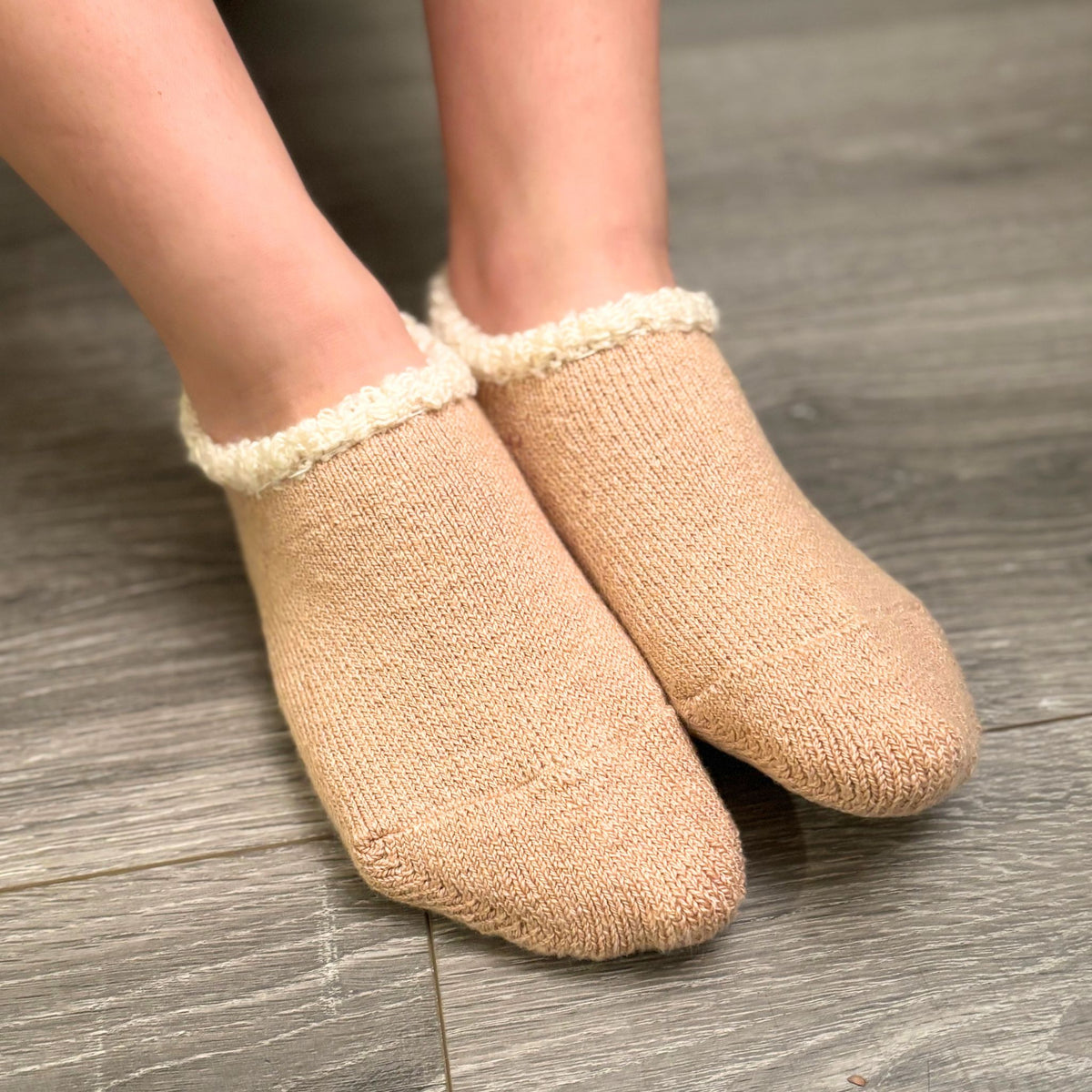 Beige slippers with white trim worn on a wooden floor