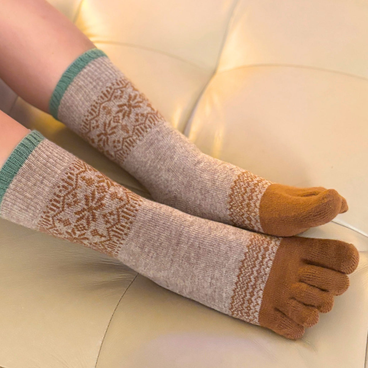 A person wearing greige with a pattern, sitting on a beige couch.