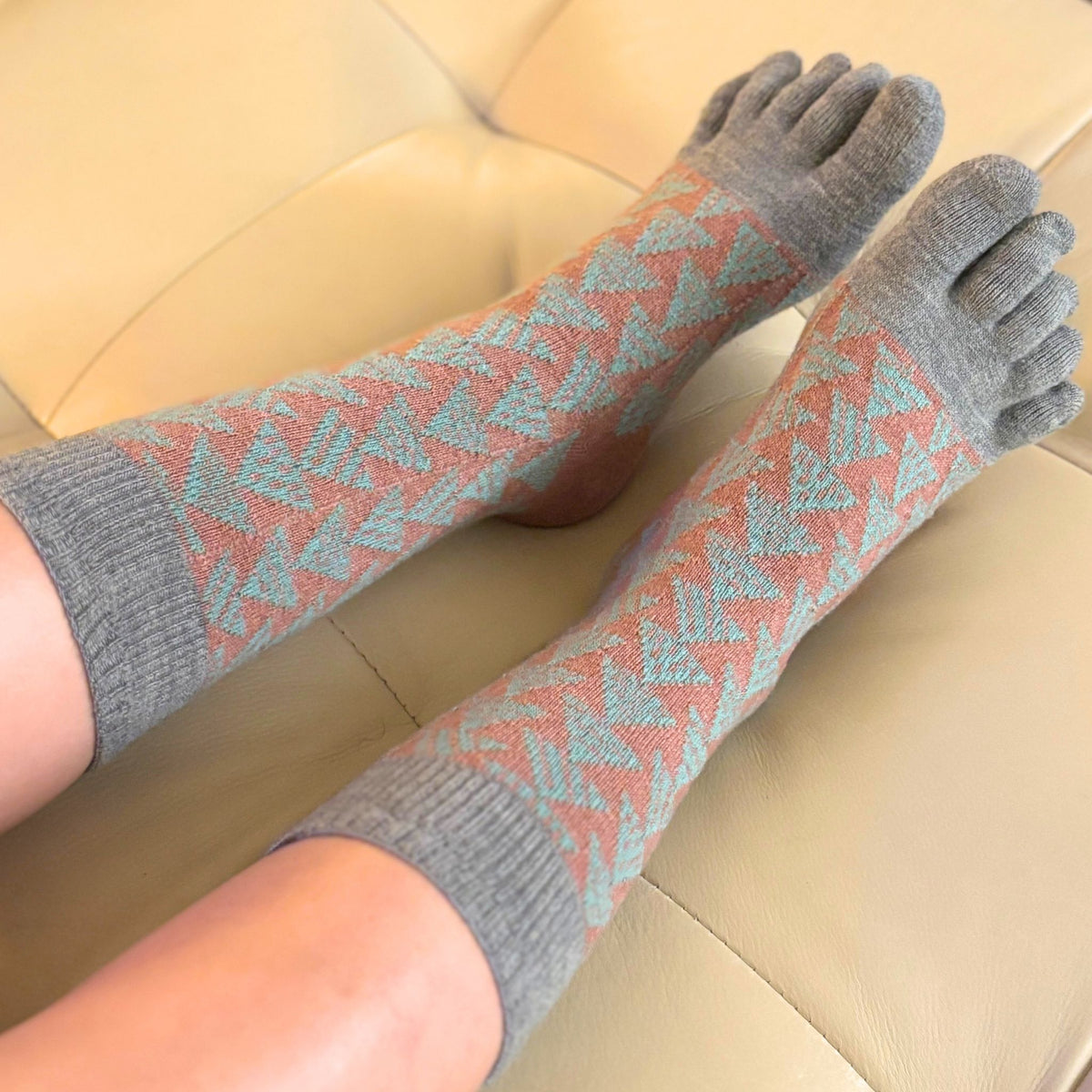 Person wearing patterned five-toe socks on a beige couch