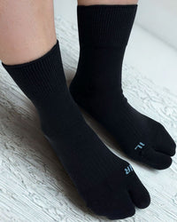 Black toe-separated socks worn on a light wooden floor