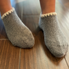 Angora Slipper Socks with anti-slip soles featuring transparent grip dots for extra safety. Each pair is handcrafted, incorporating traditional craftsmanship, and finished with cherrystone shell-shaped embroidery on the sock opening. Soft, cozy, and comfortable for ultimate foot pampering.