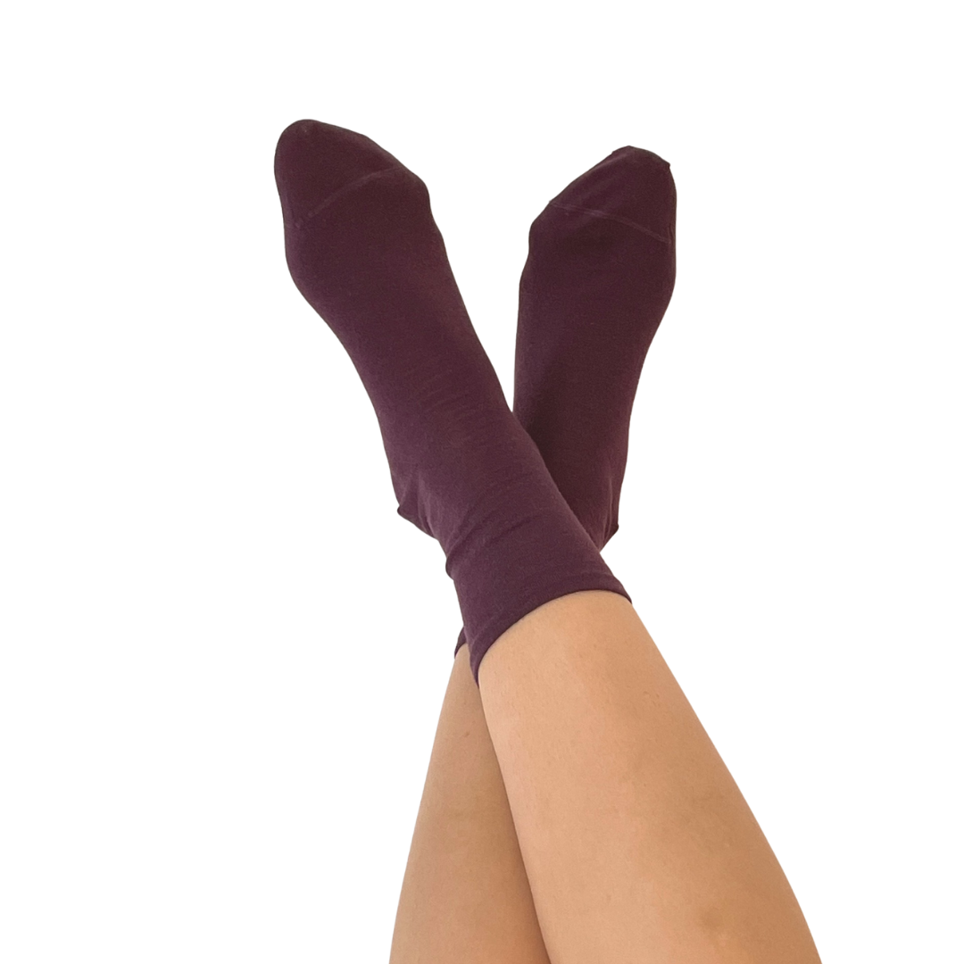 A pair of dark plum purple crew socks worn on crossed legs, shown against a solid white background.
