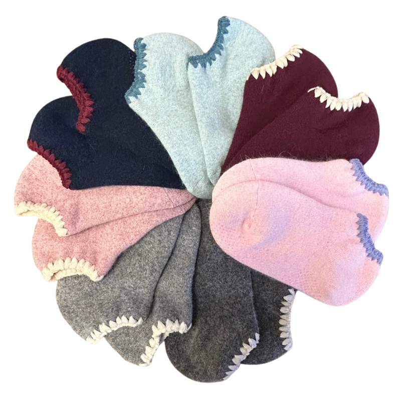 Angora Slipper Socks with anti-slip soles featuring transparent grip dots for extra safety. Each pair is handcrafted, incorporating traditional craftsmanship, and finished with cherrystone shell-shaped embroidery on the sock opening. Soft, cozy, and comfortable for ultimate foot pampering.